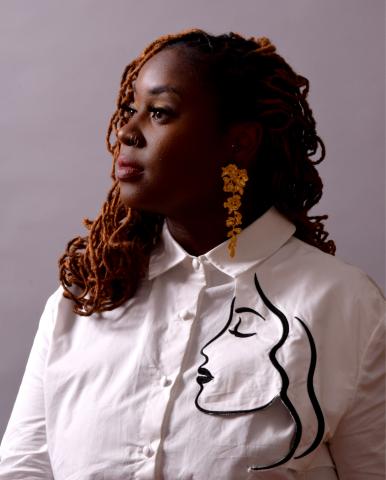 Lady Brion, seated facing a light, wearing a white shirt with a woman's facial silhouette.